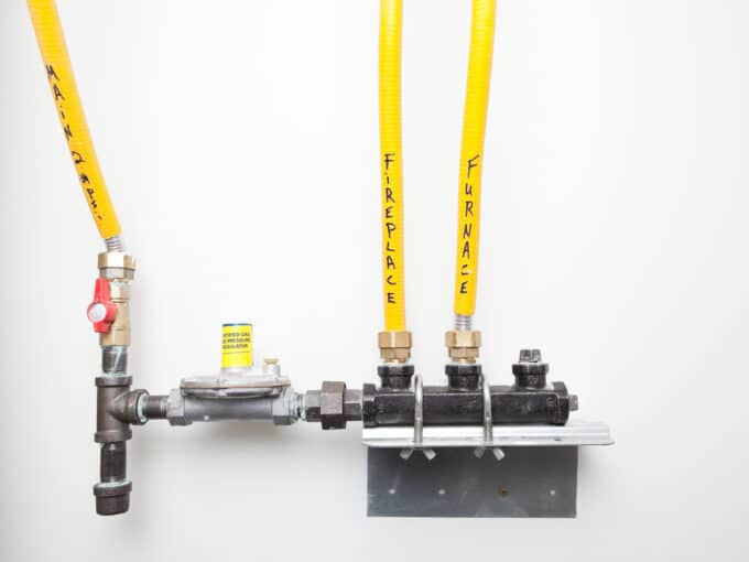 A simple house natural gas pressure regulator and manifold mounted to a wall. The main line coming into the house is on the left and the manifold distributes gas to a fireplace and furnace.